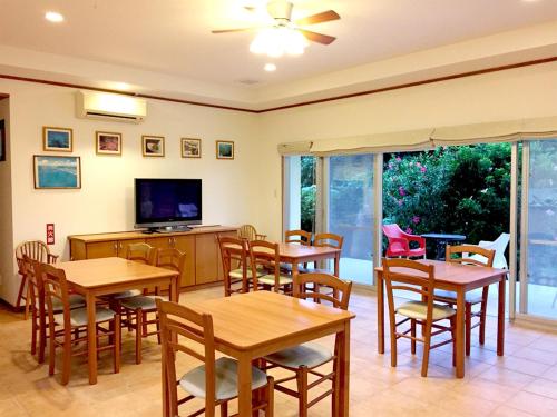 a dining room with tables and chairs and a flat screen tv at Pine Shima Resort Coral Fish in Ibaruma