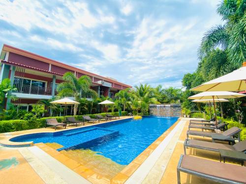 a swimming pool with chairs and umbrellas next to a building at Hatzanda Lanta Resort - SHA Extra Plus in Ko Lanta