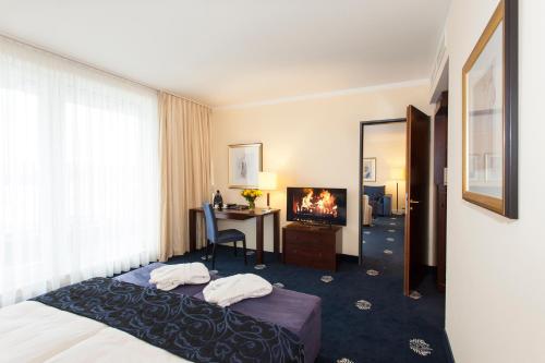 ein Hotelzimmer mit einem Bett, einem Schreibtisch und einem TV in der Unterkunft Hotel Vier Jahreszeiten Starnberg in Starnberg