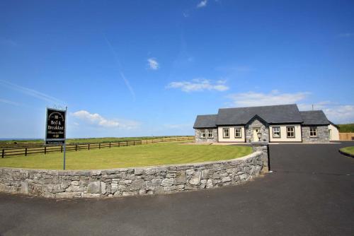 a white house with a stone wall and a sign at Cahermaclanchy House in Doolin