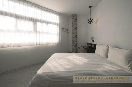 a white bedroom with a white bed and a window at Journey Hostel in Tainan