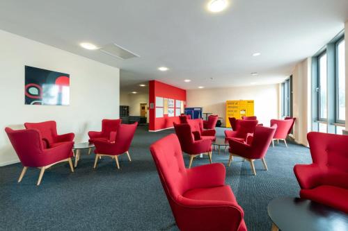 a waiting room with red chairs and tables at For Students Only Collegiate Athena Hall Ipswich in Ipswich