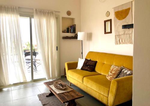sala de estar con sofá amarillo y mesa en יעלת חן Ya'alat hen, en Yeruham