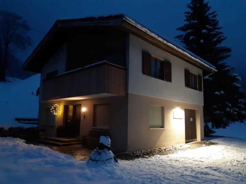 a house with a dog standing in front of it in the snow at Ferienhus Klus 415 in Mellau