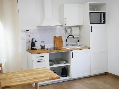 eine Küche mit weißen Schränken und einem Holztisch in der Unterkunft Studio cosy Bienvenue chez Elle in Saint-Denis-de lʼHôtel