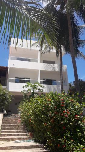 a white building with stairs and palm trees and flowers at Suíte em Japaratinga com Vista do Mar in Japaratinga