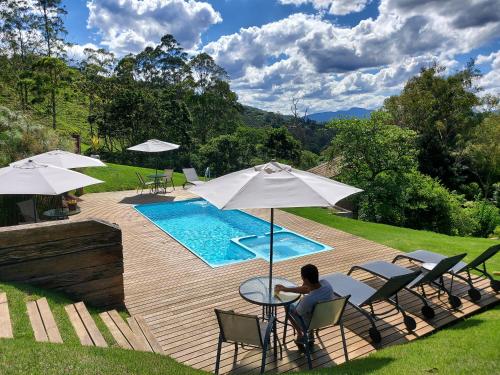 una persona sentada en una mesa con una sombrilla junto a una piscina en Pousada Reserva Nativida, en Santo Antônio do Pinhal