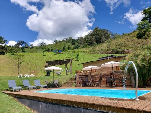 a swimming pool with chairs and umbrellas next to a hill at Pousada Reserva Nativida in Santo Antônio do Pinhal