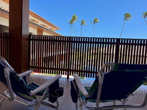 two chairs on a balcony with a fence and palm trees at Apto novo Imperia Lounge pé-na-areia Itacimirim in Itacimirim