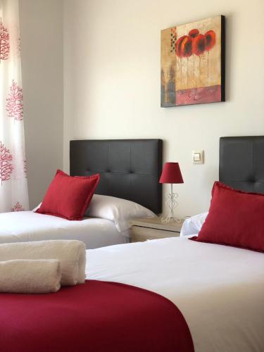 a bedroom with two beds with red pillows and a painting at Alojamientos El Chorro in Los Navalucillos