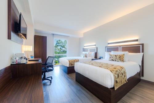 a hotel room with two beds and a desk and a television at Sleep Inn Guadalajara Galerias in Guadalajara