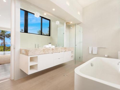 a white bathroom with a tub and a sink and a window at Kiah - nestled between Main & Belongil Beaches in Byron Bay