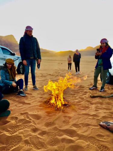 a group of people standing around a fire in the sand at Shakria Bedouin Life Camp in Wadi Rum