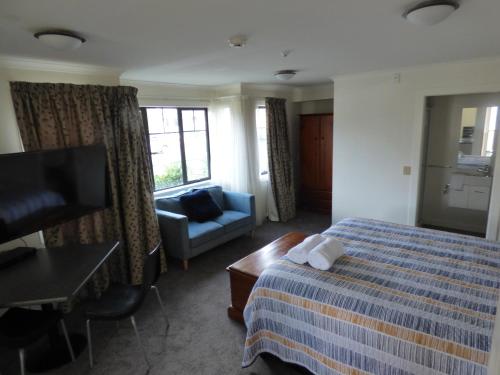 a hotel room with a bed and a chair and a television at Sahara Deluxe Studios in Dunedin