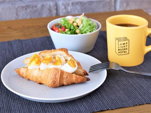 a plate with a piece of bread and a salad and a cup of coffee at LAMP LIGHT BOOKS HOTEL fukuoka in Fukuoka