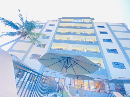 a tall building with a palm tree and an umbrella at Hotel Comster Mtwapa in Mtwapa