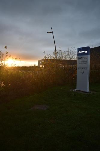 a motel sign in the grass with the sunset in the background at The Originals City, L'Haut' Aile, Coquelles-Calais Tunnel s/Manche L'HAUTAILE in Coquelles