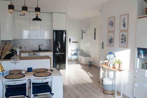 Apartament HAMPTONS Gdynia في غدينيا: مطبخ مع دواليب بيضاء وجزيرة مطبخ مع كراسي