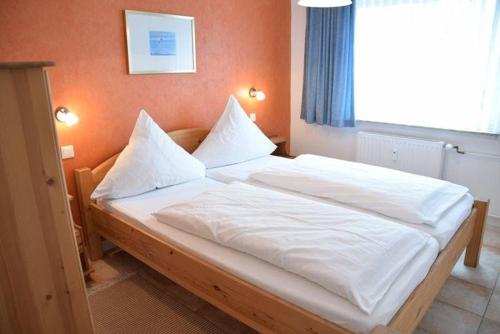 een bed met witte lakens en kussens in een kamer bij App-Stadtoase-Haus-Nordland in Westerland