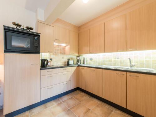 a kitchen with wooden cabinets and a microwave at Apartment Goldsands II 101 with garage by Interhome in De Haan