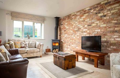 a living room with a brick wall and a flat screen tv at Hetty's Stables in Yanworth