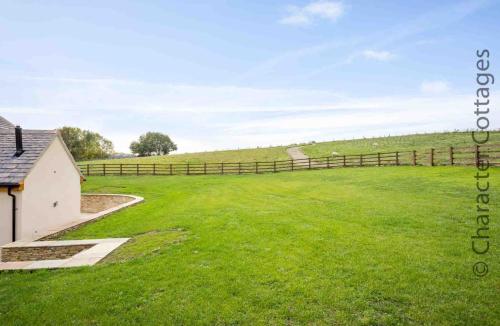 a large grassy field with a fence and a house at Hetty's Stables in Yanworth