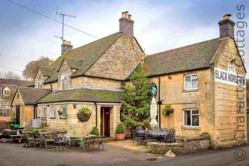 an inn with tables and chairs in front of it at Hetty's Stables in Yanworth