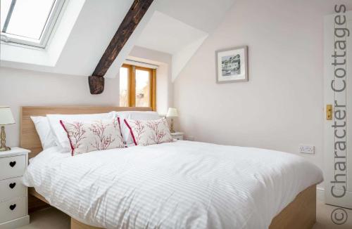 - une chambre avec un lit doté de draps blancs et d'oreillers rouges dans l'établissement Oyster Barn, à Naunton