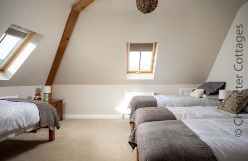 a attic bedroom with three beds and two windows at Flynn's Barn 