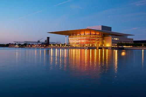 a building with its lights on in front of a body of water at City Apartment With Exposed Ceiling Beams in Copenhagen