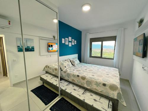 - une chambre dotée d'une paroi en verre avec un lit et un miroir dans l'établissement Home 49 I Apto pé na areia e piscina aquecida em Bertioga, à Bertioga