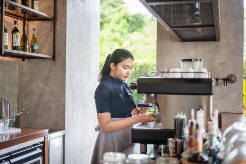 a woman standing in a kitchen preparing a drink at Kokotel Phuket Nai Yang Beach in Nai Yang Beach