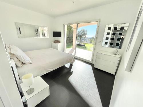 a white bedroom with a bed and a large window at Villa Le Clos des Lauriers in Roquebrune-Cap-Martin