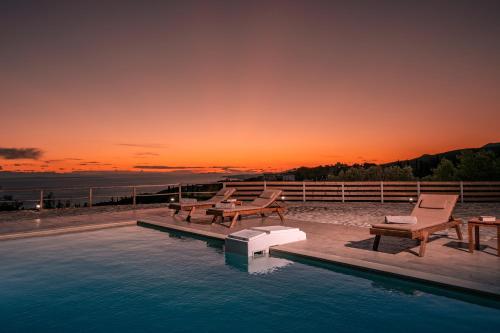 a swimming pool with chairs and a sunset in the background at Villa Foteini in Skinária