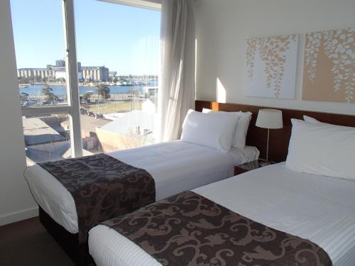 a hotel room with two beds and a large window at Newcastle Central Plaza Apartment Hotel Official in Newcastle