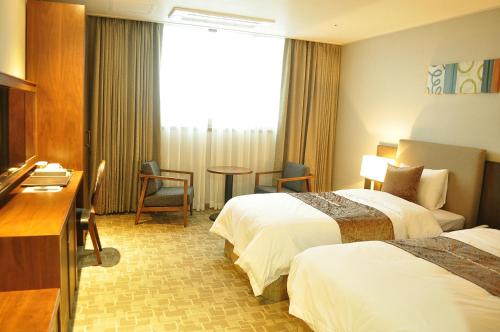 a hotel room with two beds and a desk at Hyunjin Tourist Hotel in Donghae
