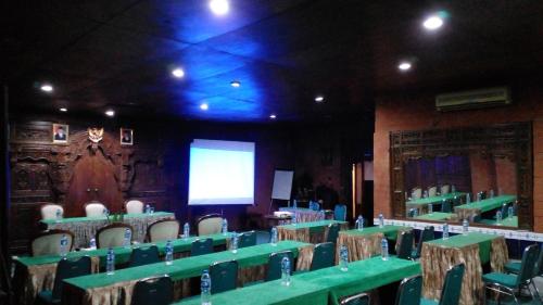 a room with green tables and chairs and a screen at Hotel Bifa Yogyakarta in Yogyakarta