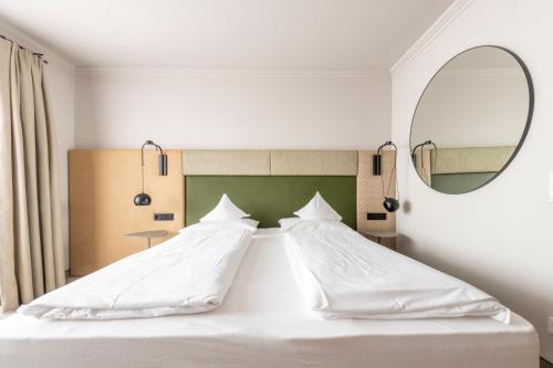 a bedroom with a large white bed with a mirror at Hotel Jakob in Fuschl am See