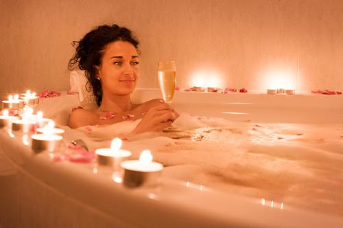 een vrouw in een bad met een glas champagne bij Seehotel Sparer in Appiano sulla Strada del Vino