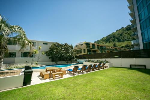 a resort with a pool and chairs and a building at Beaumont Apartments in Mount Maunganui