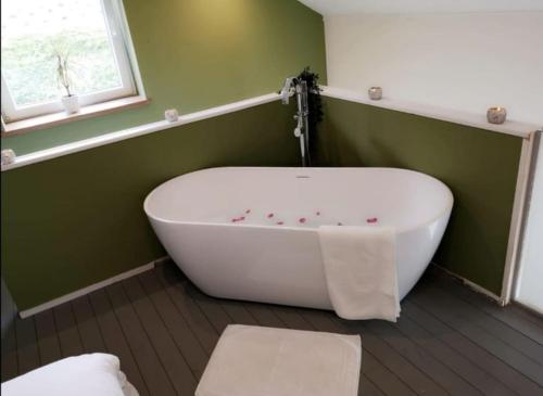 a white bath tub in a green bathroom with a window at Ô'bel Écrin in Aubel