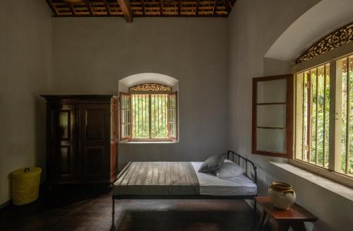 a bedroom with a bed and two windows at Gileemale Walawwa & Estate in Ratnapura