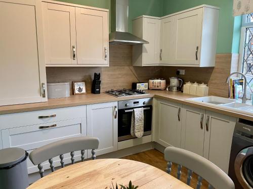 a kitchen with white cabinets and a wooden table at Bronte Bungalow - In Beautiful Bronte Country! in Oxenhope