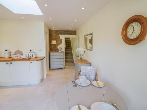 a kitchen with a table and a clock on the wall at Bumble Cottage in Warwick