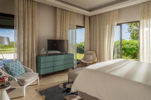 a bedroom with a large bed and a tv and windows at Four Seasons Resort Mauritius at Anahita in Beau Champ