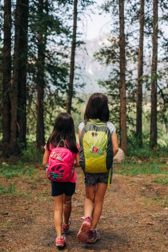 two girls with backpacks walking down a forest trail at Mountaineer Lodge in Lake Louise