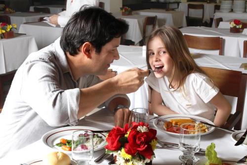 a man and a girl sitting at a table eating food at Hotel Majestic in Águas de Lindóia