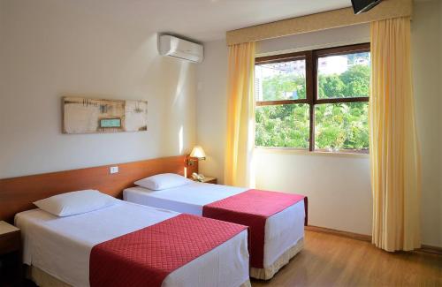 two beds in a hotel room with a window at Hotel Majestic in Águas de Lindóia