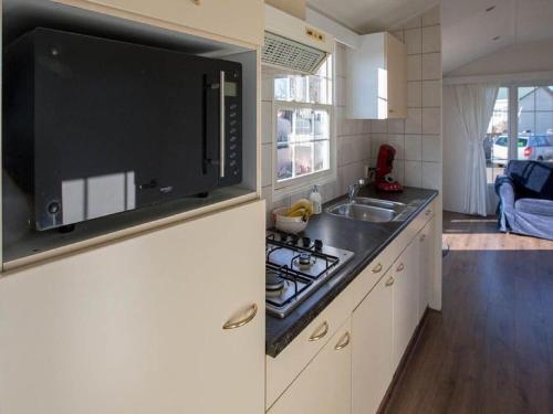 a kitchen with a sink and a microwave above a stove at Detached chalet on a holiday park with two terraces, near Alkmaar in Hensbroek