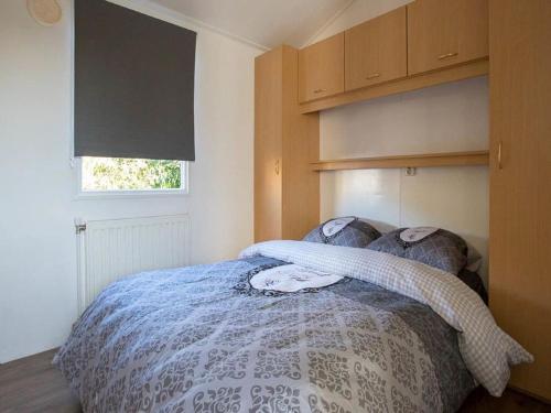 a bedroom with a bed with a blue comforter and a window at Detached chalet on a holiday park with two terraces, near Alkmaar in Hensbroek